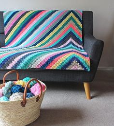 a crocheted blanket sitting on top of a couch next to a basket filled with yarn