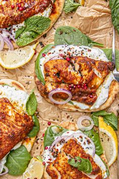 three chicken burgers with spinach, onions and lemon slices on paper wrappers