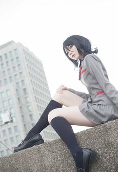 a woman sitting on top of a stone wall next to tall buildings