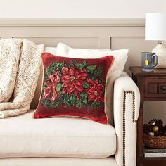 a white couch with a red and green pillow on top of it next to a lamp