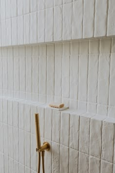 two toothbrushes are on the edge of a white tiled wall with gold handles