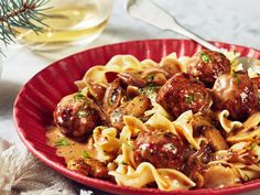 a red bowl filled with pasta and meatballs next to a glass of olive oil