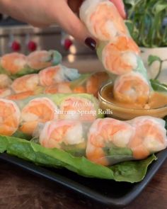 someone is dipping shrimp in sauce on top of some lettuce leaves and other vegetables