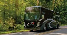 a black bus driving down the road in front of some trees and bushes on both sides