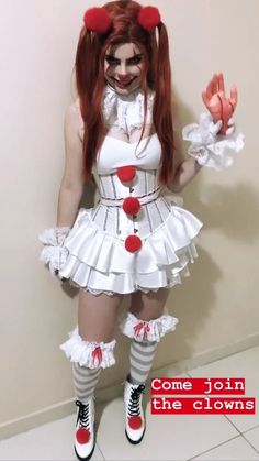 a woman dressed up as a clown with long red hair and white dress is standing in front of a wall