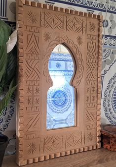 an intricately carved wooden frame sits on a table next to a potted plant