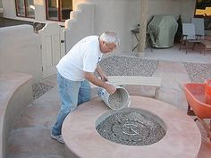 an older man is pouring cement into a fire pit in front of a house with patio furniture