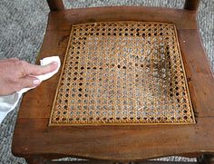 a person cleaning a wooden chair with a cloth on the seat and one hand holding a rag