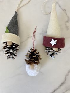 three pine cones with christmas decorations hanging from them on a marble counter top next to a candy cane