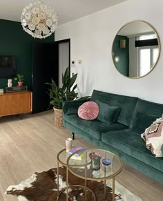 a living room with green velvet couches and a round mirror hanging on the wall