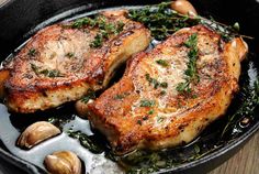 two pork chops in a skillet with mushrooms and herbs on the side, ready to be cooked