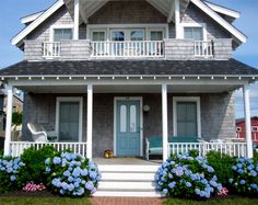 a gray house with blue hydrangeas in the front yard and steps leading up to it