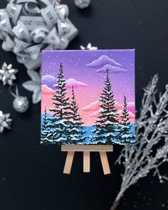 an easel with a painting on it next to some snow and christmas decorations in the background