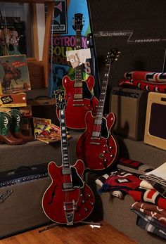 two red guitars sitting on top of a wooden floor next to an amplifier and guitar case