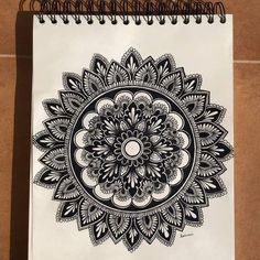 a spiral notebook with an intricate black and white design on the front, sitting on a brown surface