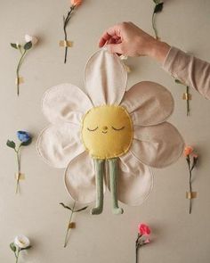 a person holding a flower shaped object in front of flowers on the wall with their hands