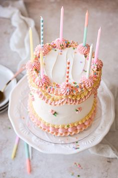 a white cake with pink frosting and candles on it sitting on top of a plate