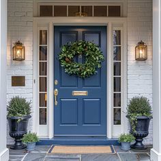 a blue front door with two potted plants and a wreath on the side entrance