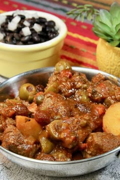 a metal bowl filled with meat and vegetables next to a bowl of black olives