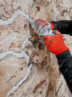 a person wearing red gloves is climbing up a rock wall with his hands on the edge