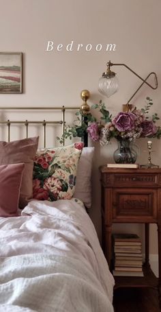 a bed with white sheets and pink flowers on the headboard next to a night stand