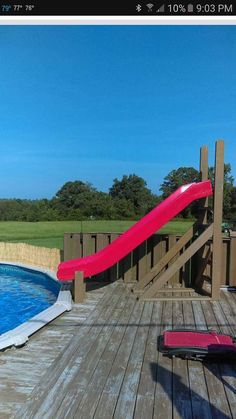 a red slide in the middle of a wooden deck next to a pool with blue water