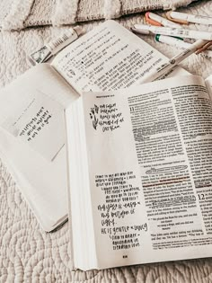 an open bible laying on top of a bed next to crayons and markers