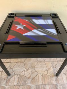 a black table with a flag painted on the top and two legs, sitting on a tile floor