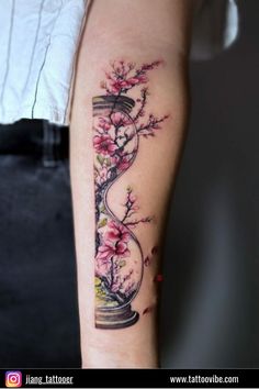 a woman's arm with flowers and an hour - glass tattoo on the left forearm