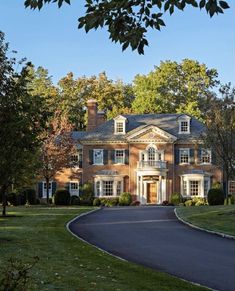 a large brick house with lots of windows and trees in the front yard, surrounded by lush green grass