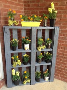 a wooden shelf filled with potted plants next to a brick wall