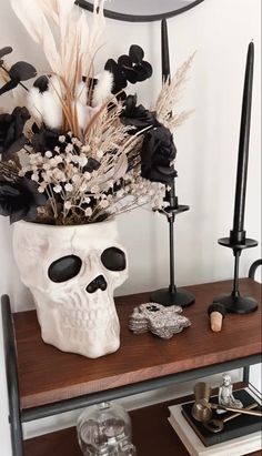 a skull vase with flowers in it sitting on a shelf next to candles and other items