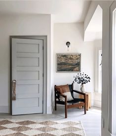 a room with a chair, rug and painting on the wall next to an open door