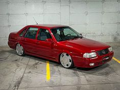 a red car parked in a parking lot next to a white wall and yellow lines