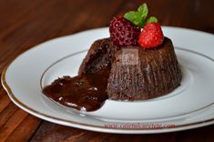 a piece of chocolate cake on a white plate with some strawberries and chocolate sauce