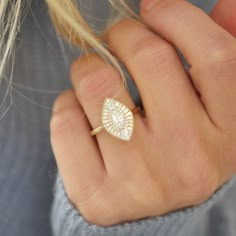 a woman's hand wearing a gold ring with an oval shaped diamond in the center