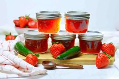 several jars of jam with strawberries and cucumbers next to them on a cutting board