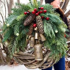 a woman carrying a wreath with bells and pine cones on her shoulders in the snow