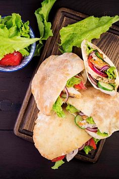 two pita sandwiches with lettuce and tomatoes on a wooden tray next to strawberries