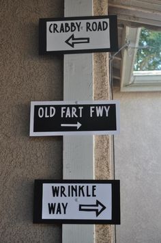 street signs pointing in different directions on a wall with a window behind them and the words crabby road, old fart fwy, wrinkle way