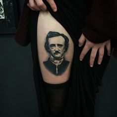 a person with a black and white portrait tattoo on their thigh, holding onto the leg