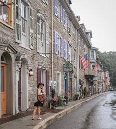 a woman is standing on the sidewalk in front of some buildings with flags and flowers