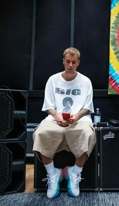 a man sitting on top of a chair in front of two amps and a painting