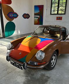 an old car painted with multicolored squares in a garage next to paintings on the wall