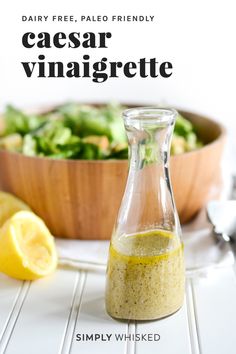 a glass bottle filled with dressing next to a bowl of salad and lemon wedges