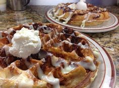 two plates with waffles covered in syrup and ice cream sitting on a table