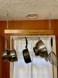 pots and pans hanging from hooks on a window sill in front of curtains