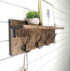 a wooden shelf with three hooks and two potted plants on the ledge above it