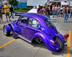 a purple car parked in a parking lot next to other cars and people standing around