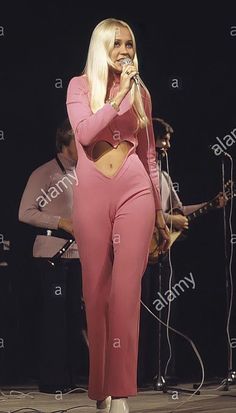 lady in pink outfit singing on stage with band playing behind her